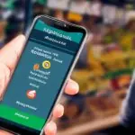 A close-up of a smartphone displaying the M-PESA Ethiopia app interface, with an AI-powered chatbot providing real-time financial advice. The vibrant Ethiopian marketplace background features cinematic lighting casting soft shadows on the screen a…