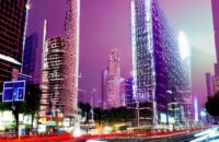 A futuristic smart city street at night where autonomous vehicles, hovering drones, and holographic ads showcase the vibrant integration of 6G connectivity and AI in daily life.