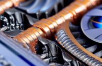 A high-performance NVIDIA graphics card rests on a matte black desk, illuminated by cinematic blue and orange lighting that highlights its metallic heatsink fins and glowing green status indicators.