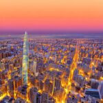 A twilight skyline of a modern Moroccan city blending traditional arches with futuristic glass skyscrapers. Holographic displays float over a bustling digital plaza, symbolizing the convergence of historic heritage and advanced technology.