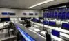 Dimly lit military command center featuring glowing server racks and digital data walls. Operators monitor network topologies under cool blue lighting, illustrating advanced cyber defense infrastructure and technological superiority.