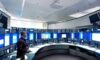 Futuristic security command center with analysts monitoring large curved screens displaying real-time certificate trust metrics and automated renewal dashboards under soft blue lighting, highlighting human oversight in PKI management.