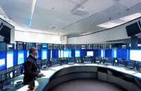Futuristic security command center with analysts monitoring large curved screens displaying real-time certificate trust metrics and automated renewal dashboards under soft blue lighting, highlighting human oversight in PKI management.