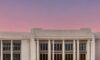 High‑resolution photorealistic view of the Pentagon’s white marble façade bathed in a dramatic sunset, with faint holographic AI circuitry patterns glowing across the building, illustrating the convergence of defense and technology under cinematic…