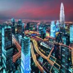 Neon‑lit futuristic city at dusk with towering skyscrapers, holographic ads, drones, and translucent data streams. A diverse group in cyberpunk attire interacts with floating holographic interfaces, reflecting awe. The scene blends physical and di…