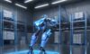A humanoid robot navigates a modern automated warehouse with cool blue lighting, highlighting precision engineering and efficiency alongside a human worker.