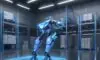 A humanoid robot navigates a modern automated warehouse with cool blue lighting, highlighting precision engineering and efficiency alongside a human worker.