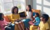 A diverse group of children laughing and playing educational games on tablets while sitting together on a cozy sofa in a sunlit modern living room.