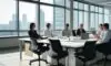 A diverse team of professionals laughing and collaborating during a creative brainstorming session around a large glass table in a modern, sun-lit corporate office.