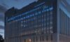 A cinematic shot of a modern government building in Washington D.C. at dusk, featuring holographic data streams and glowing blue circuit patterns overlaid on the stone architecture to symbolize the integration of AI and governance.