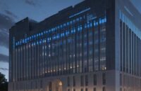 A cinematic shot of a modern government building in Washington D.C. at dusk, featuring holographic data streams and glowing blue circuit patterns overlaid on the stone architecture to symbolize the integration of AI and governance.