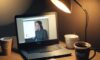 Dimly lit home office at night with a modern laptop glowing on a wooden desk, surrounded by scattered papers, a coffee mug, and headphones, illuminated by warm amber lamp light in a cinematic atmosphere of late-night work.