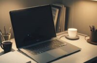 A cozy home office desk featuring a laptop displaying a terminal window with code, a notebook with a pen, and a warm cup of coffee under a soft desk lamp.