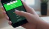 A close-up of a hand holding a smartphone displaying a minimalist security verification screen with an "Enter Code" button and a green checkmark.